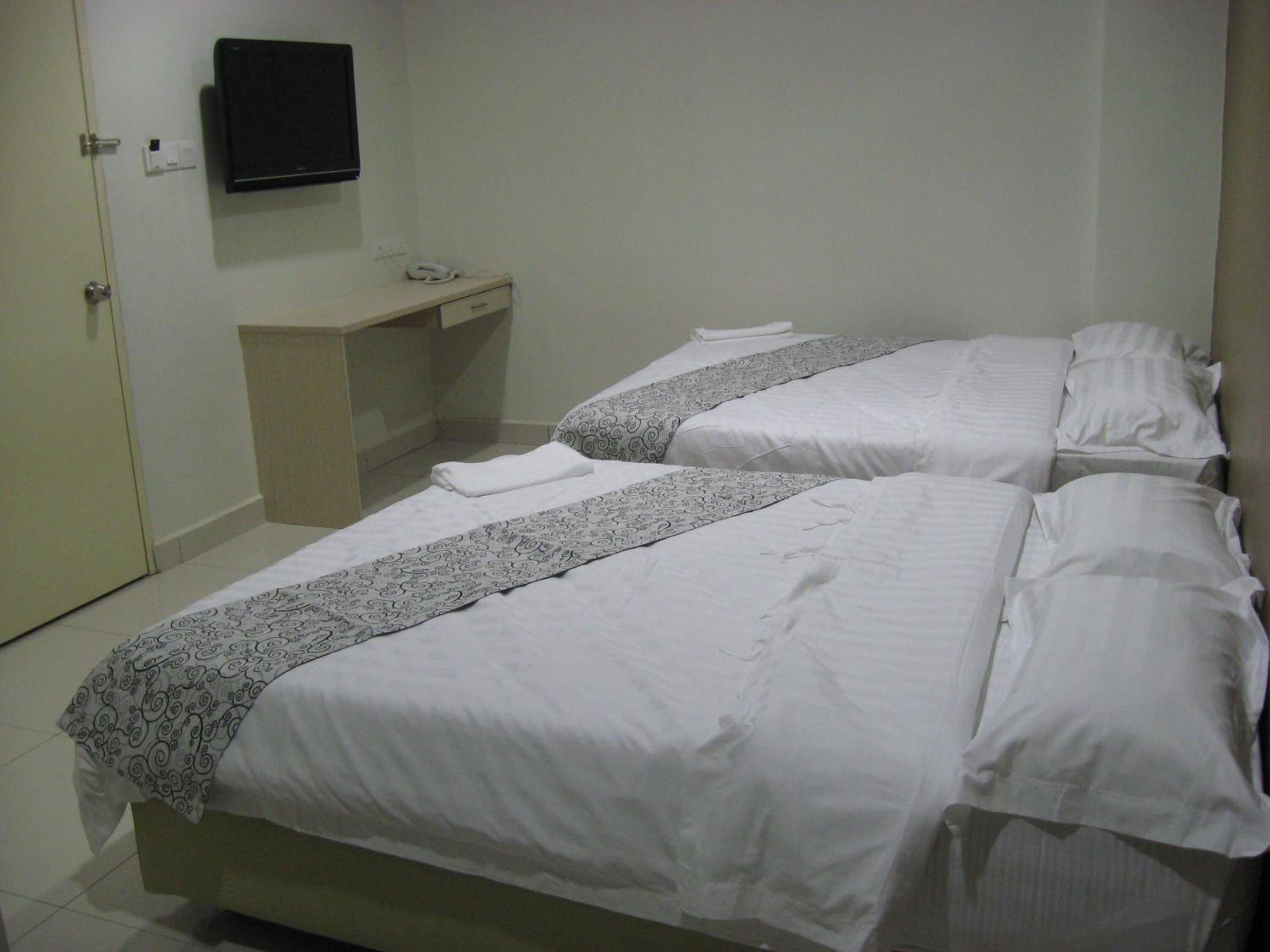 A hotel room with two beds, a bedside table, a TV mounted on the wall, and a door.