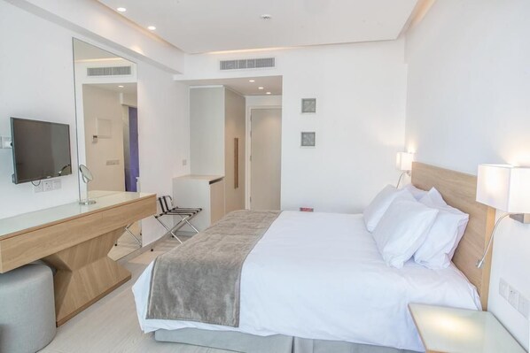 A hotel room with a bed, bedside table, lamp, desk with chair, and a television. - Kokkinos Boutique Hotel (Paralimni)