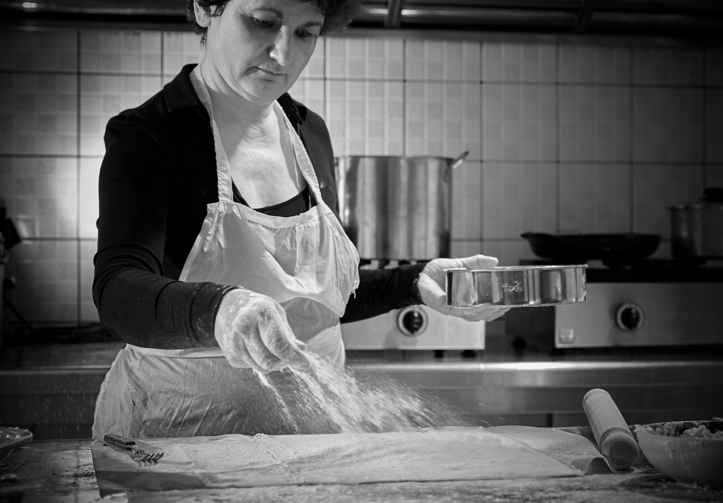 Una persona in cucina, con un grembiule, che maneggia un contenitore di metallo.