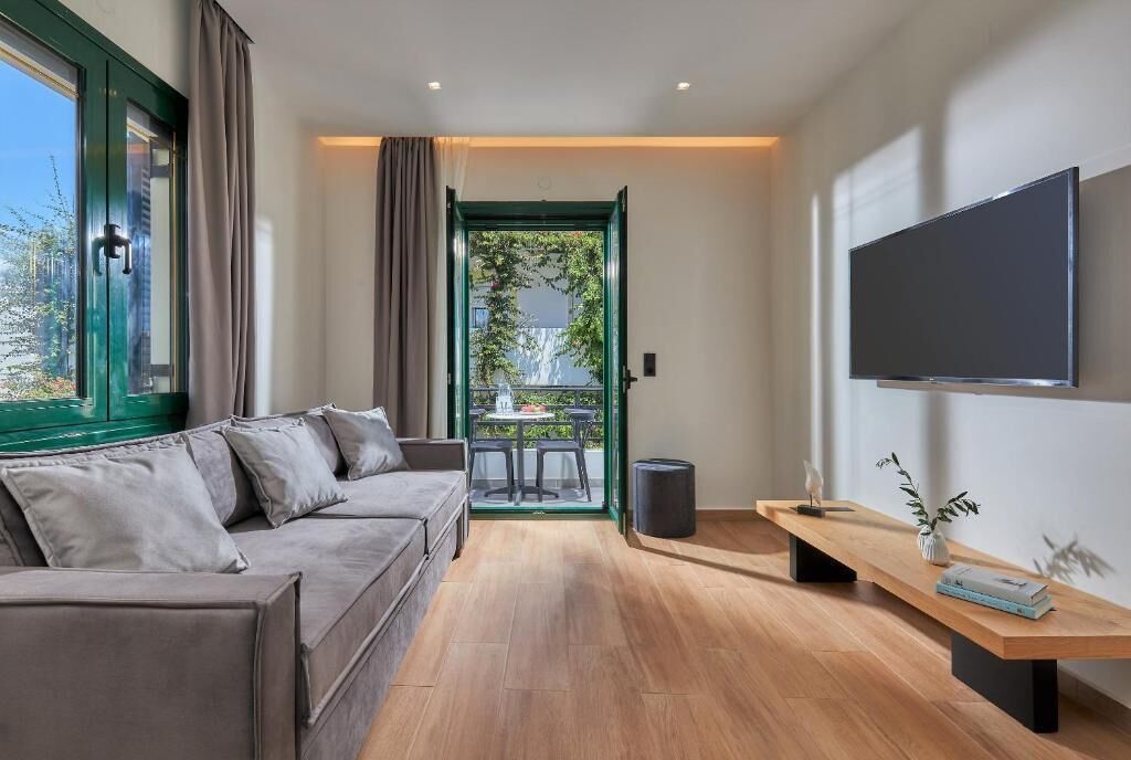 Ein modernes Wohnzimmer mit einer Couch, einem Flachbildfernseher, einer Holzbank und Blick durch eine Glastür auf einen Außenbereich.