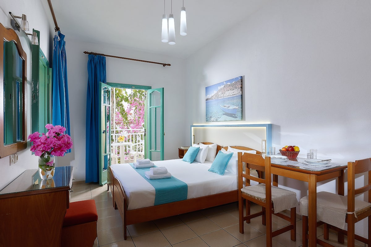 A hotel room with a bed, a desk with a chair, a vase of flowers, and a painting on the wall.