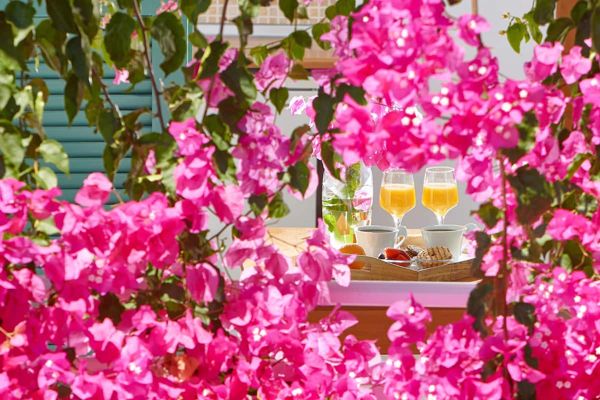 A breakfast table with orange juice, a cup, and pastries, surrounded by pink flowers.