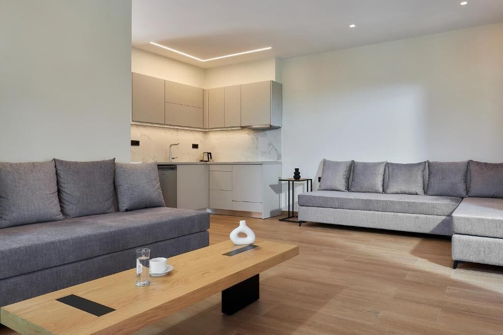 A modern living room with two grey sofas, a wooden coffee table, and a kitchen in the background.