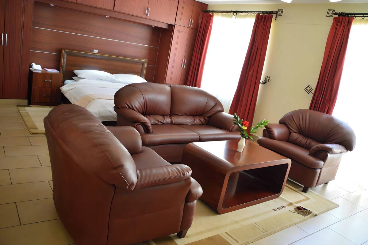 A modern hotel room with a large bed, a sofa set, and a coffee table.