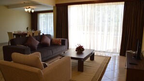 A living room with a sofa, armchair, coffee table, and a dining area with chairs and a table.