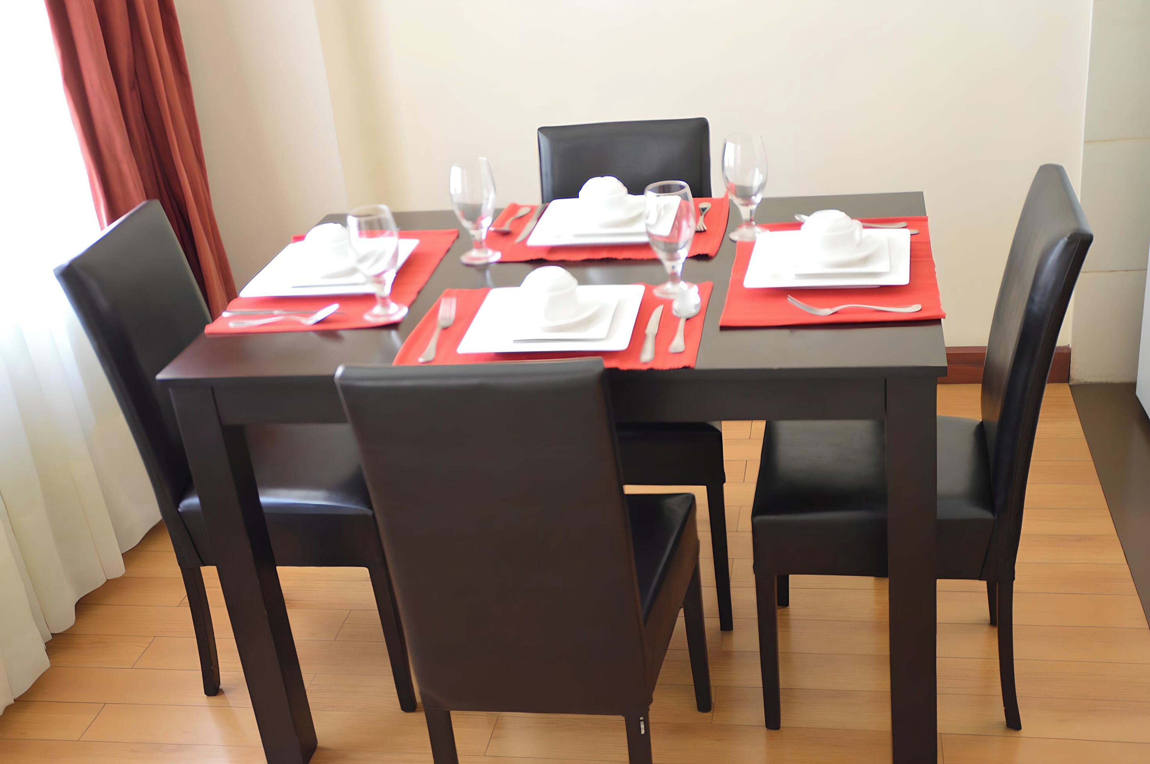A dining table set for four with red placemats, white napkins, and clear glassware.