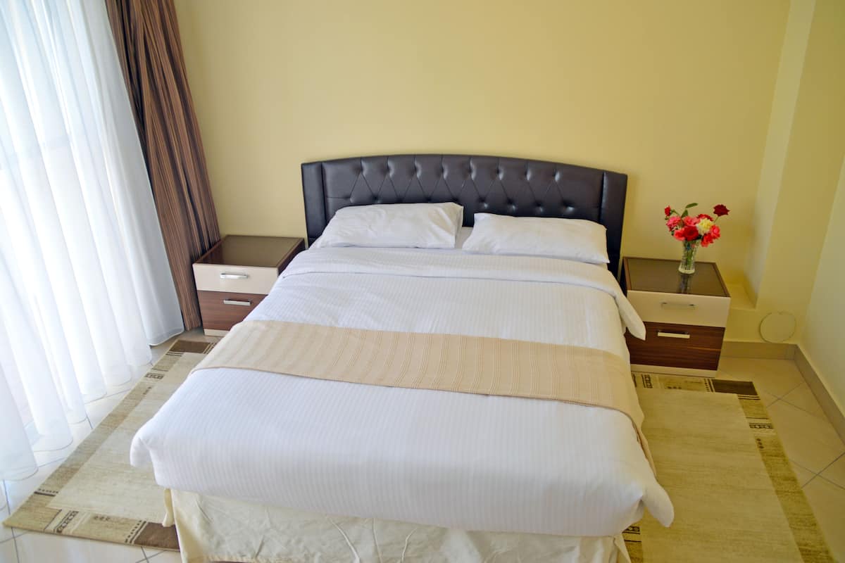 A neatly made bed with white linens, a dark headboard, and a bedside table with a vase of flowers.