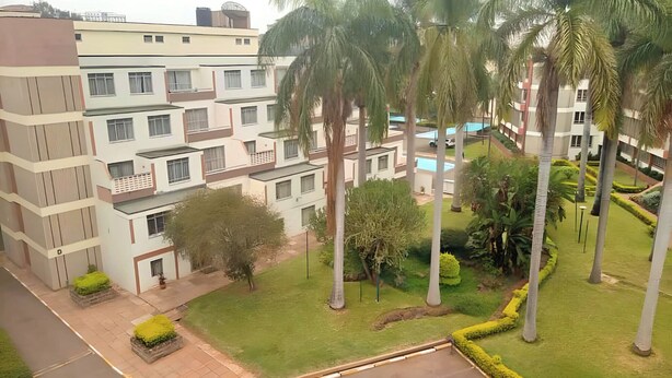 A multi-story residential building with balconies, a swimming pool, and well-maintained gardens with palm trees.