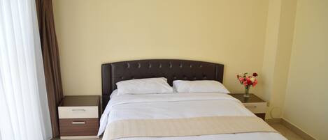 A neatly made bed with white linens, a dark headboard, and a bedside table with a vase of flowers.
