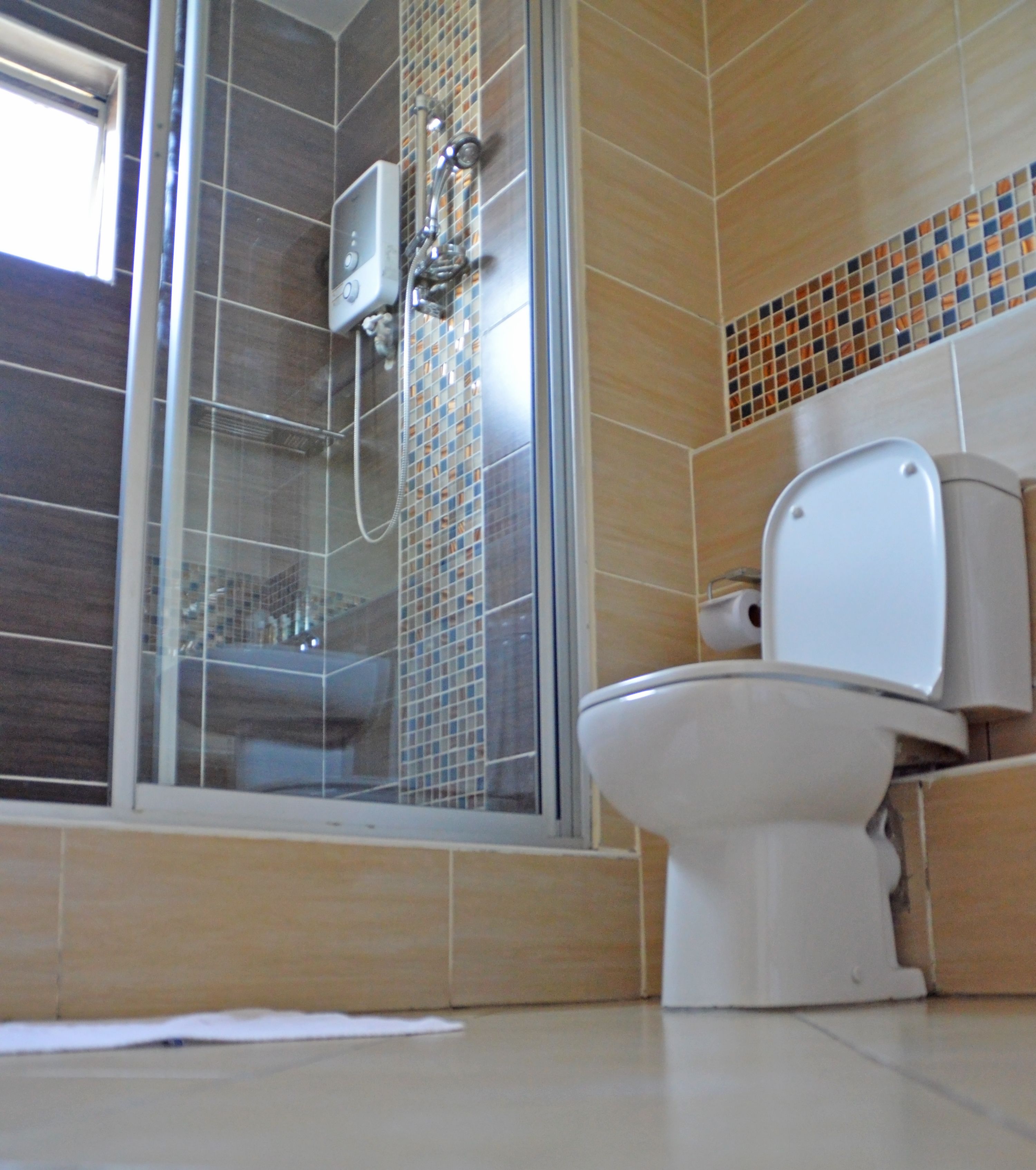 A bathroom with a glass-enclosed shower, a toilet, and a tiled floor.