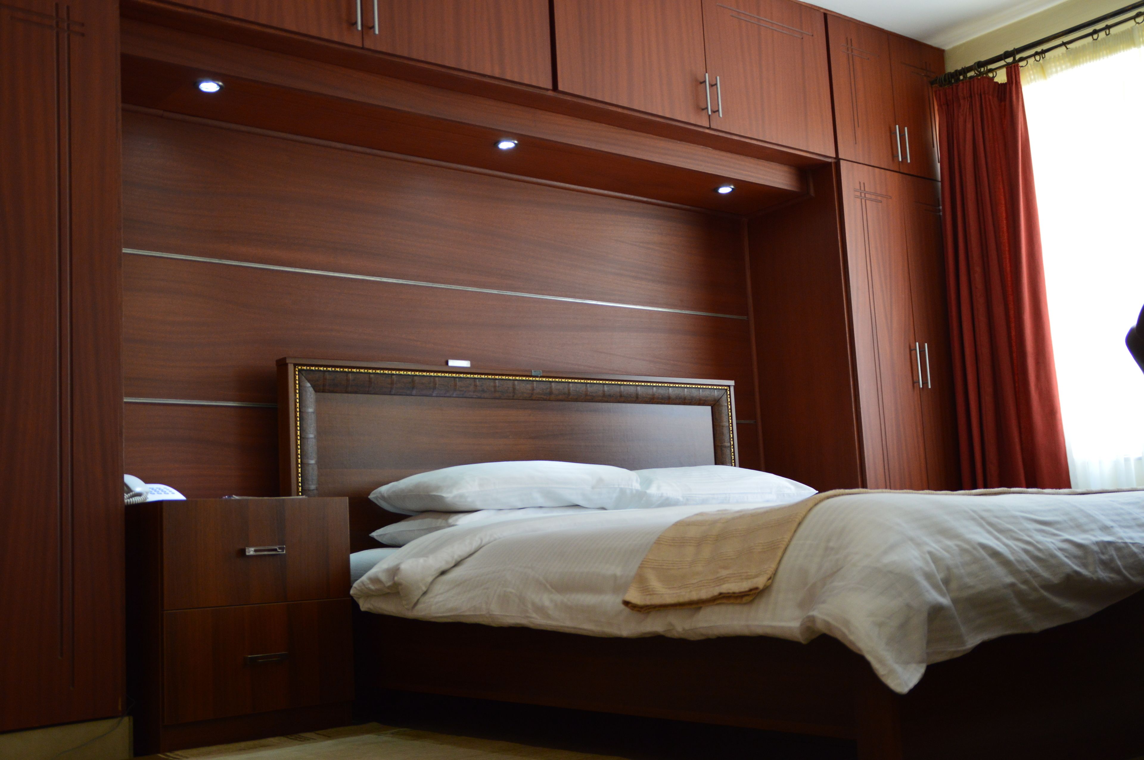 Een net opgemaakt bed met witte lakens in een kamer met houten kasten en een hoofdbord.