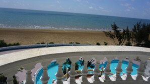 A pool with a white balustrade, a beach view, and a clear sky.