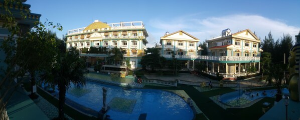 A large hotel with multiple buildings, a swimming pool area, and a bridge connecting different sections.
