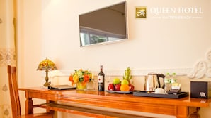 A hotel room with a wooden desk, a TV mounted on the wall, and a tray with fruits and a bottle of wine.