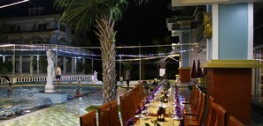A pool area with a statue, a dining setup with tables and chairs, and a building with a statue of a pharaoh.