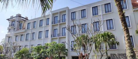 Un hotel de varios pisos con diseño moderno, que cuenta con balcones y un jardín bien cuidado con diversas plantas.