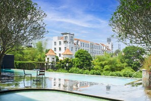 A swimming pool with a chair, surrounded by lush greenery and a large building with multiple balconies in the background. - eL Hotel Malang (Malang)