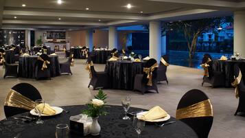 A banquet hall with round tables set for dining, featuring black tablecloths and gold chair sashes.