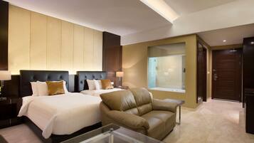 Two large beds with white linens and brown pillows, a leather armchair, and a glass coffee table.