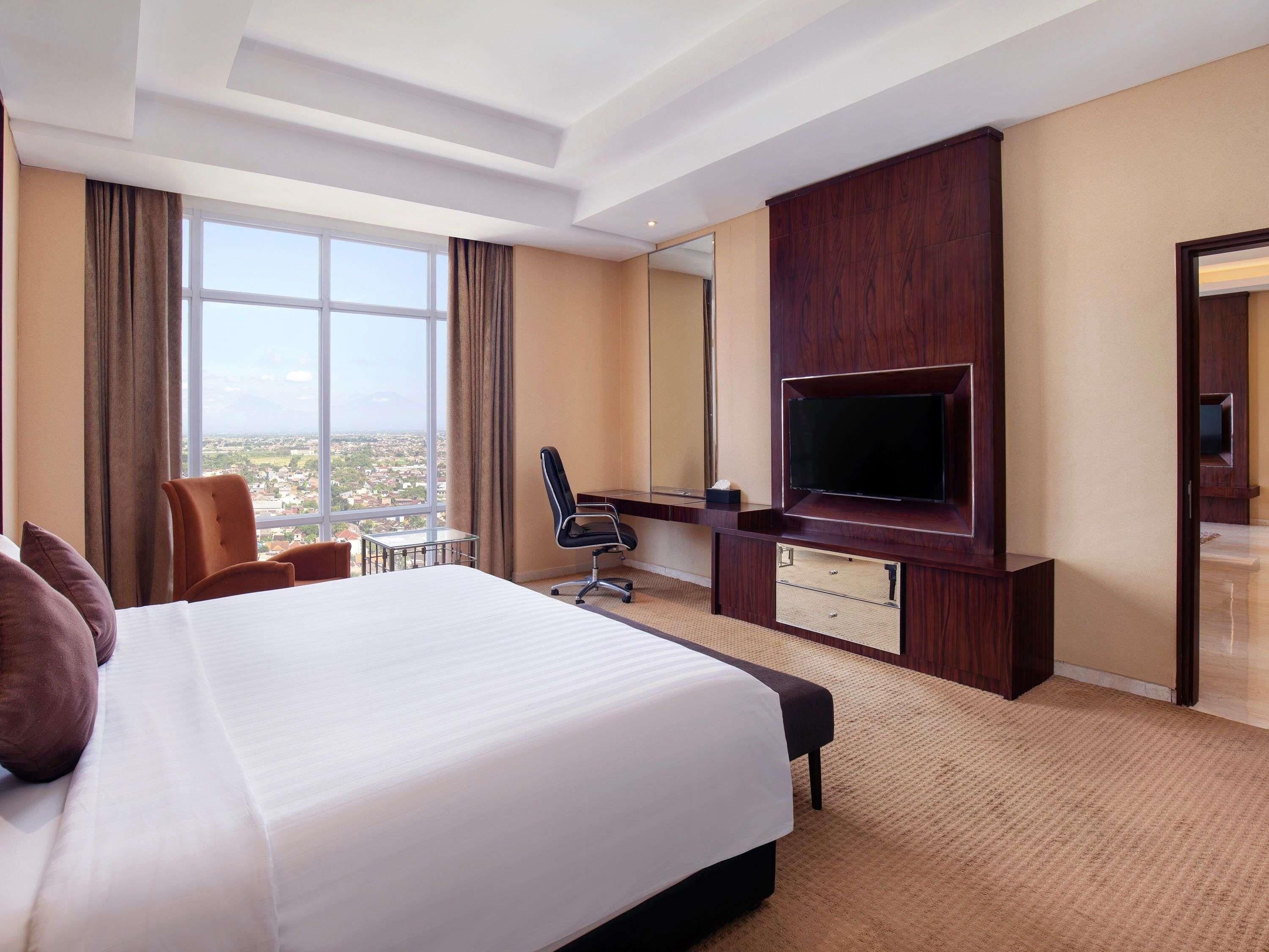 Habitación de hotel con una cama grande, un escritorio con silla, un televisor y vistas a la ciudad.