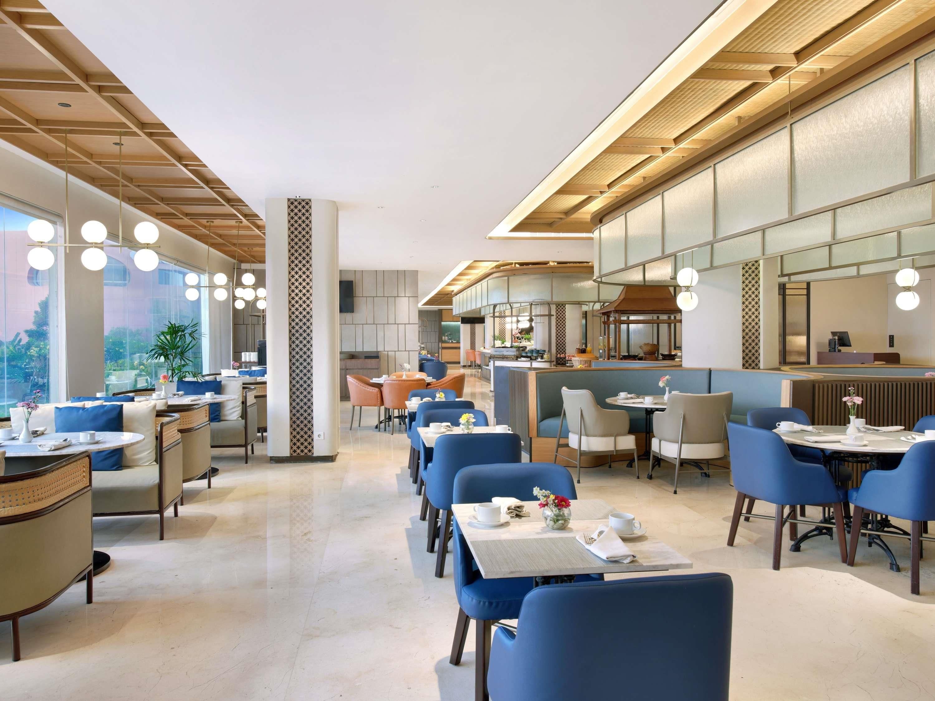 Een modern restaurant met ronde tafels, blauwe stoelen en een bar in het midden.