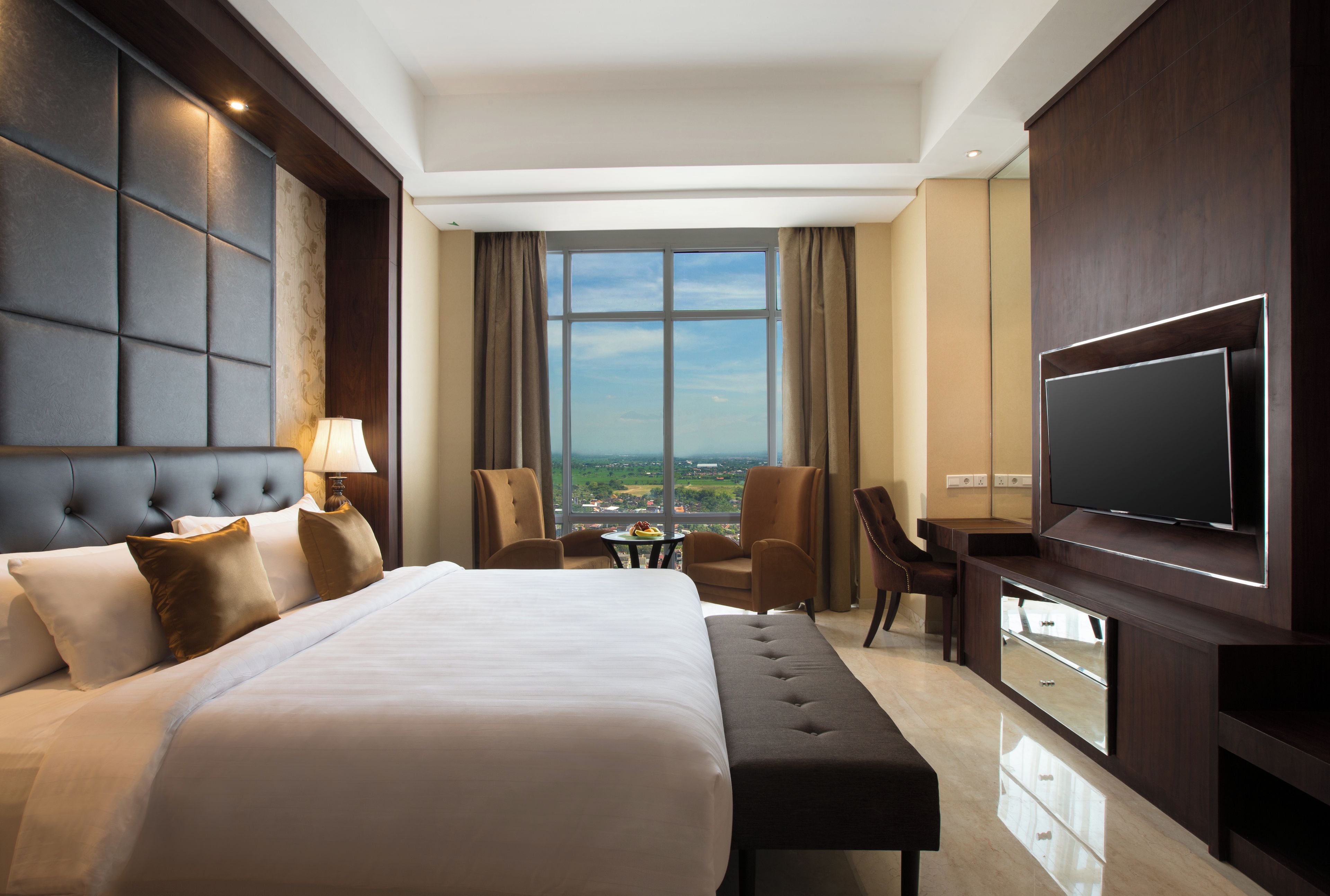 A hotel room with a large bed, a desk, a television, and a view of the city.