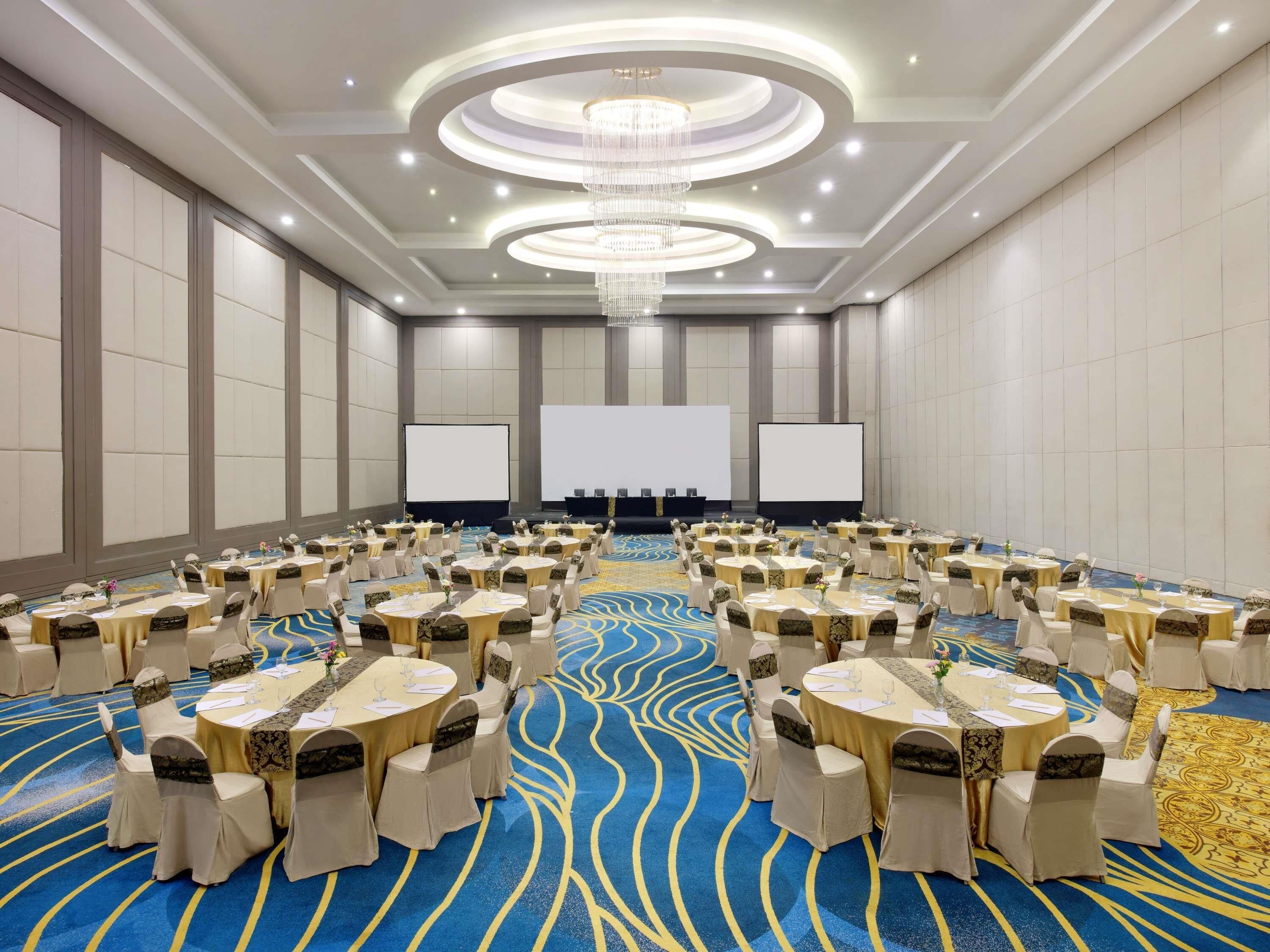 A conference room with round tables, chairs, a large screen, and a chandelier.