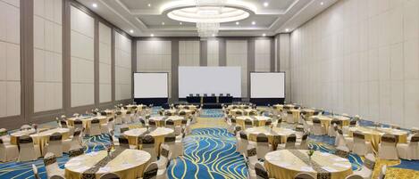 A conference room with round tables, chairs, a large screen, and a chandelier.