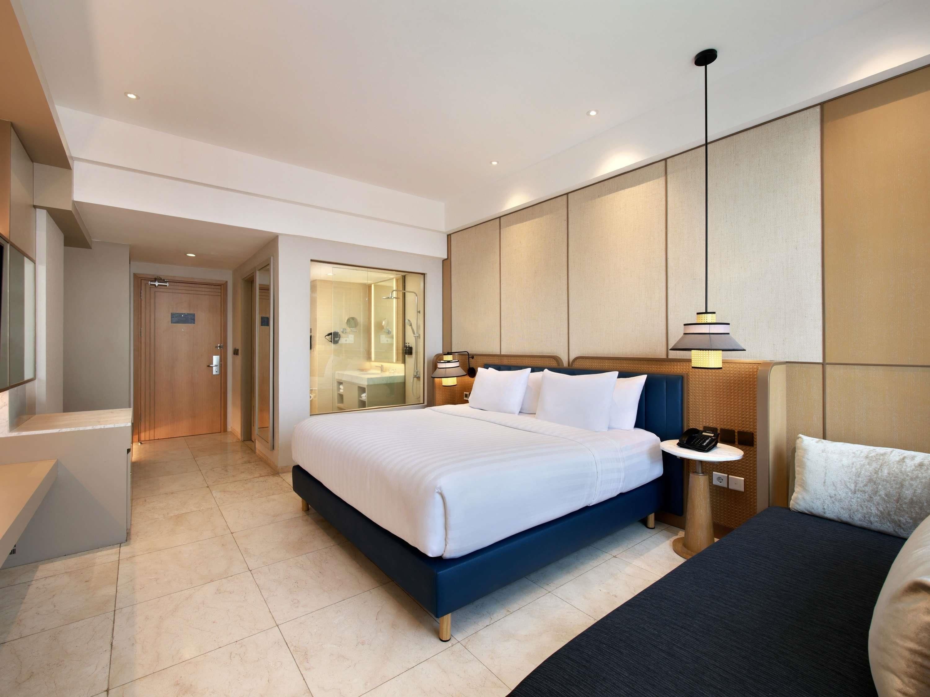 Una habitación de hotel con una cama grande, mesitas de noche, un escritorio, un espejo y una zona de ducha.