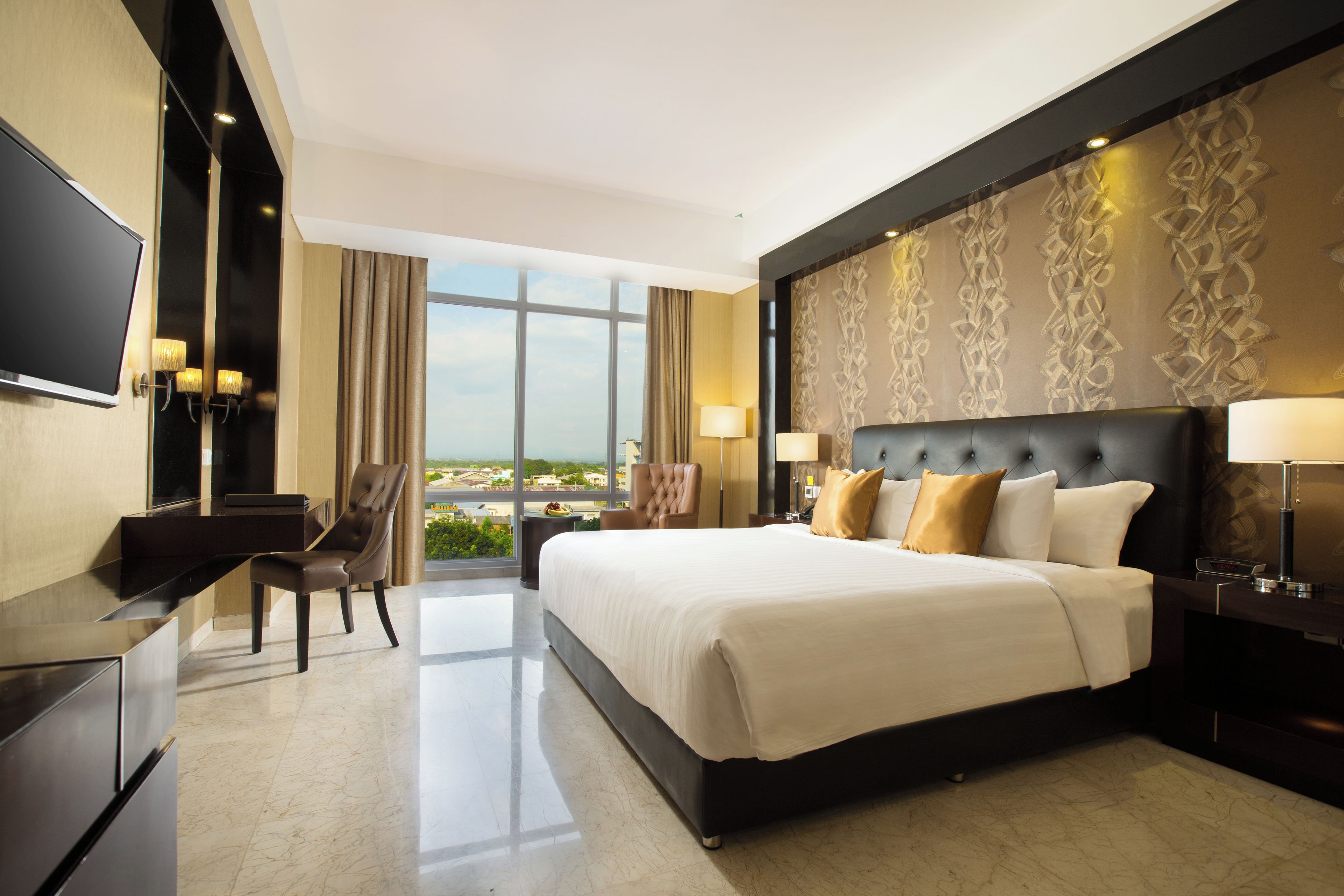 Habitación de hotel con una cama grande, un escritorio, una silla, un televisor y vistas a la ciudad.