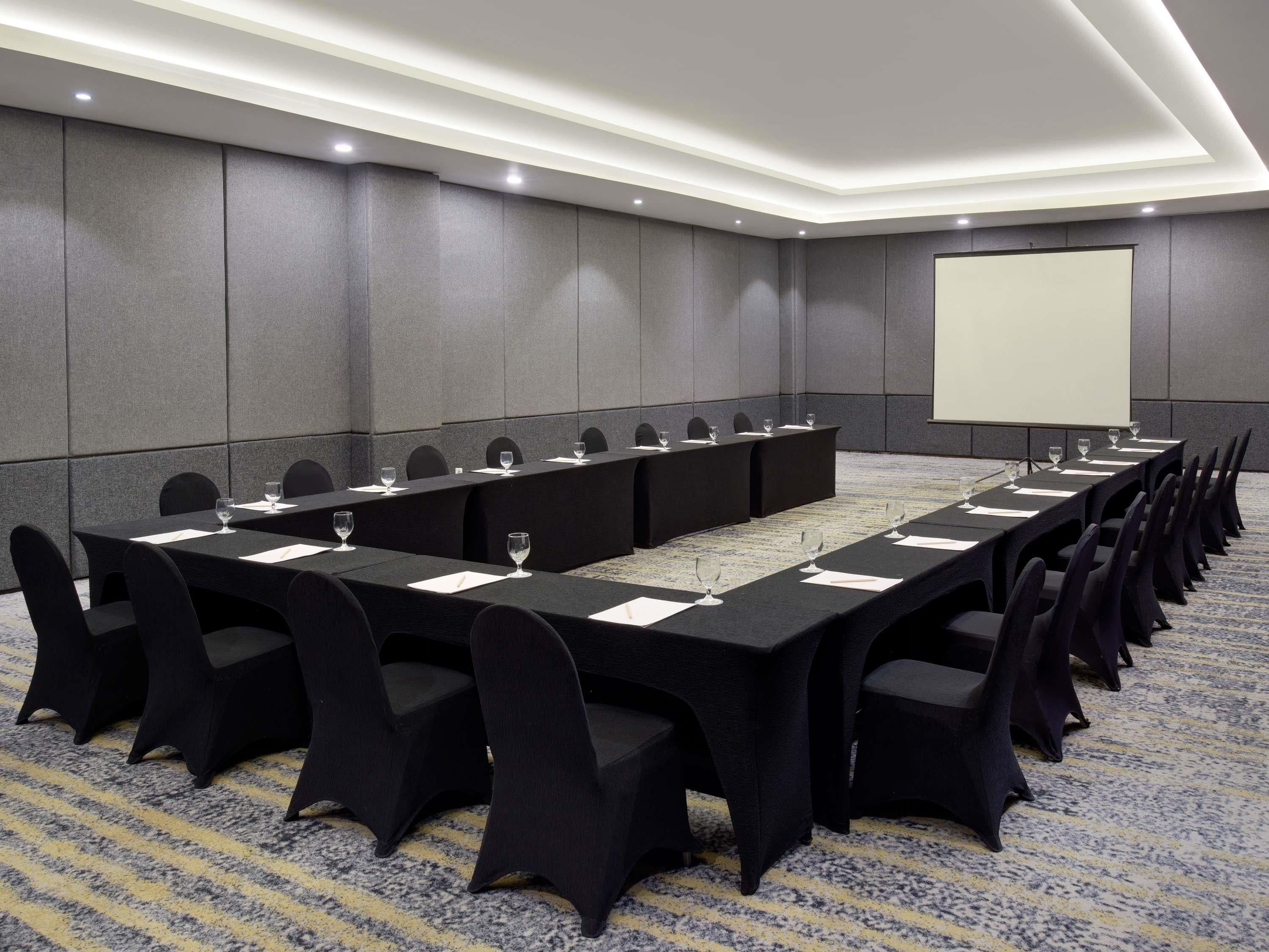 A conference room with a long table, chairs, and a projector screen.