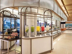 A modern hotel buffet area with a variety of food options and a self-serve drink station. - Grand Mercure Solo Baru (Grogol)