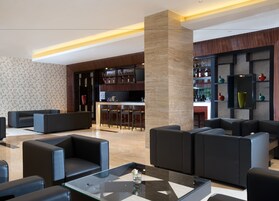 Un área de descanso moderna con sofás de cuero, una mesa de centro de vidrio y una zona de bar con estantes llenos de botellas.