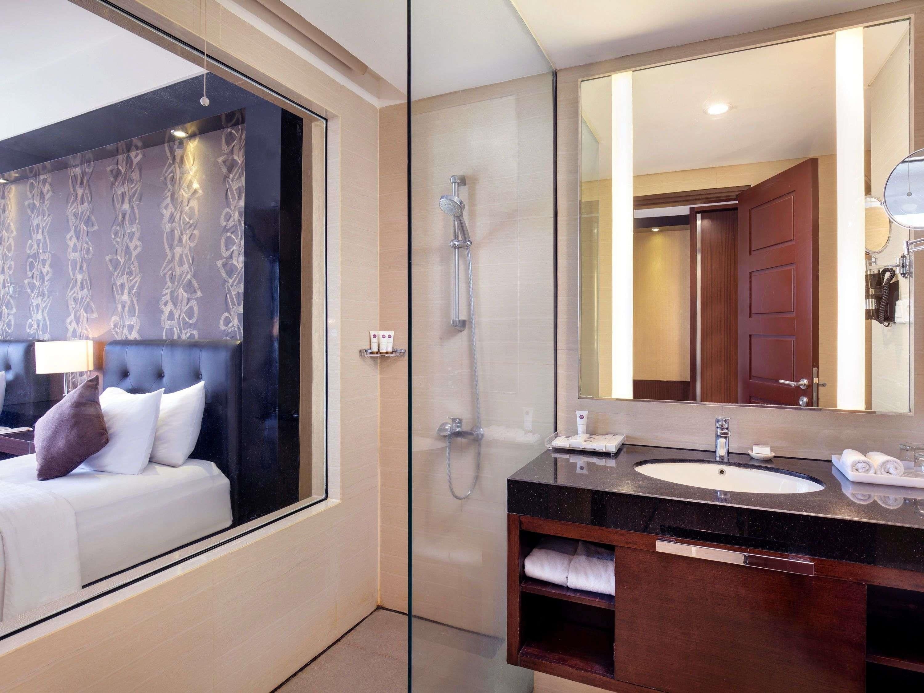 A modern bathroom with a glass shower enclosure, a large mirror, and a dark wood vanity with a sink and towel rack.