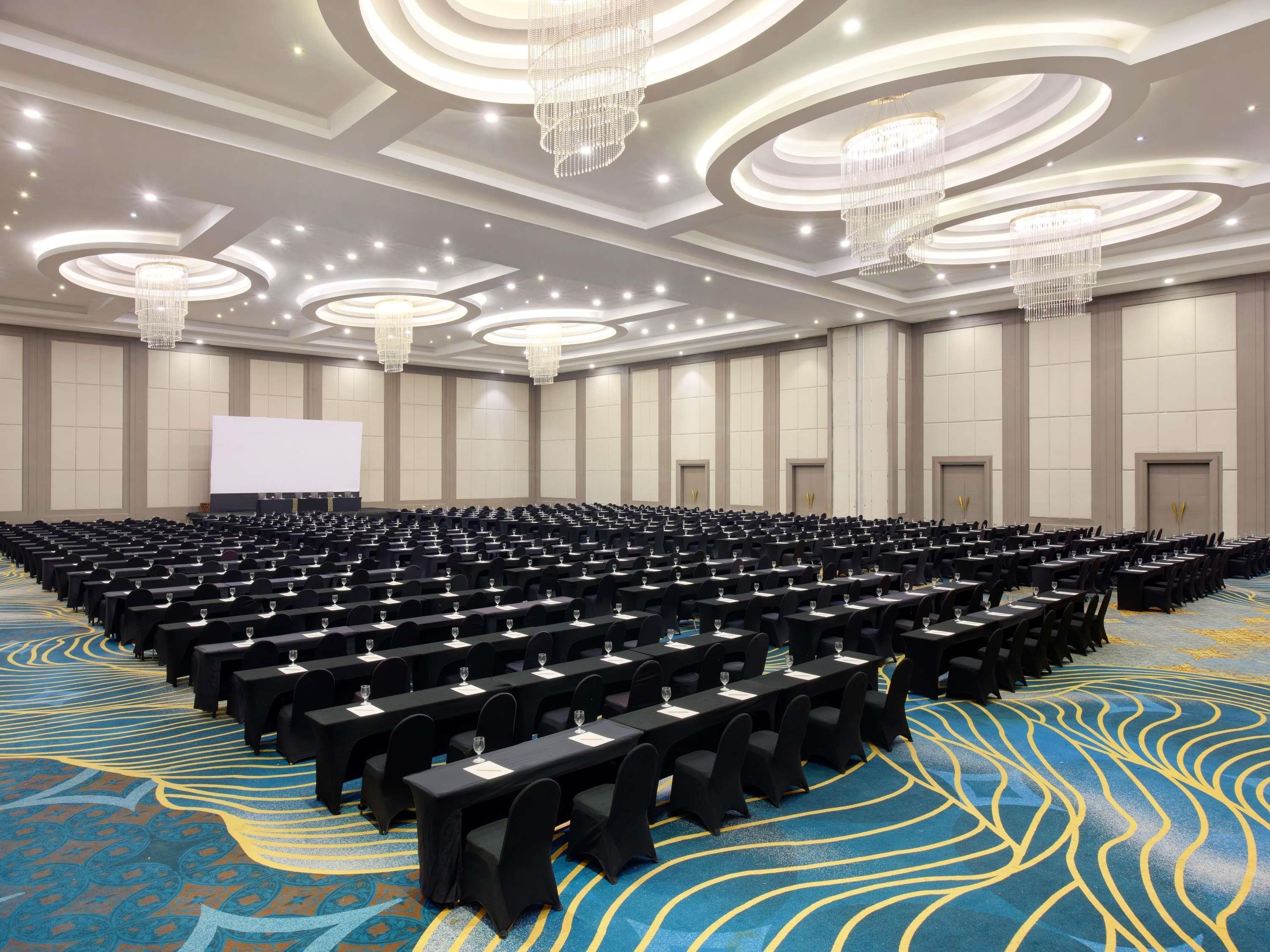 Un salón de conferencias con filas de mesas, una pantalla grande y candelabros.
