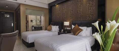A hotel room with two beds, a sitting area, a desk, and a bathroom.