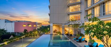 A hotel pool area with a clear view of the pool, lounge chairs, and a building with multiple windows.