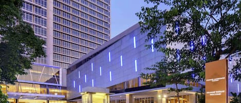 A modern hotel with a large entrance, a prominent sign, and a parking area.