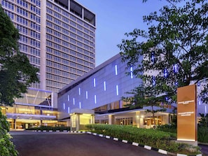 A modern hotel with a large entrance, a prominent sign, and a parking area. - Grand Mercure Solo Baru (Grogol)