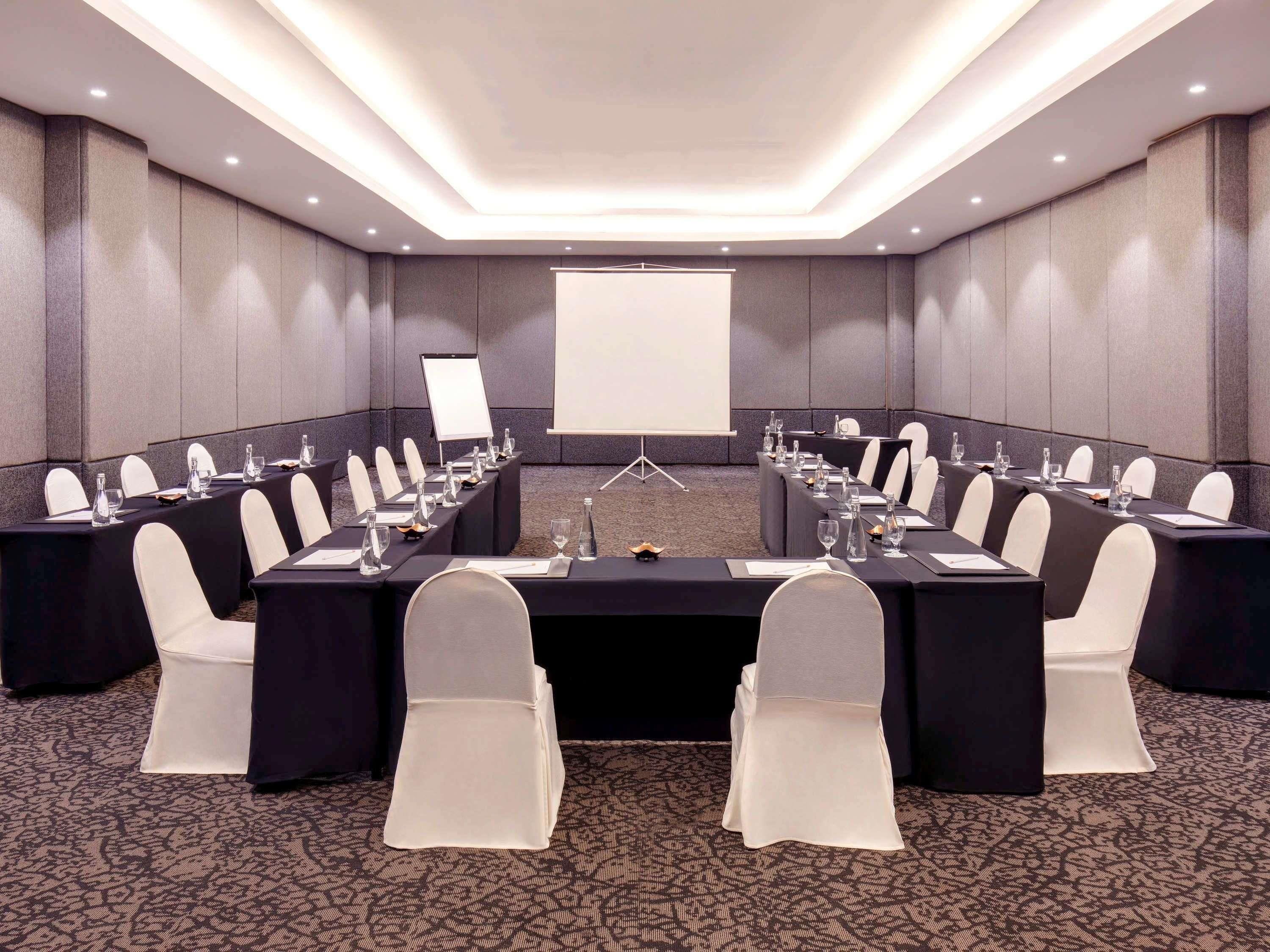 A conference room with a long table, chairs, and a projector screen.