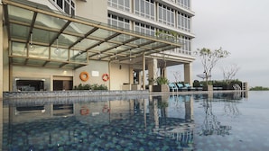 A modern hotel with a glass-enclosed pool area, outdoor seating, and a lifebuoy on the wall. - Grand Mercure Solo Baru (Grogol)