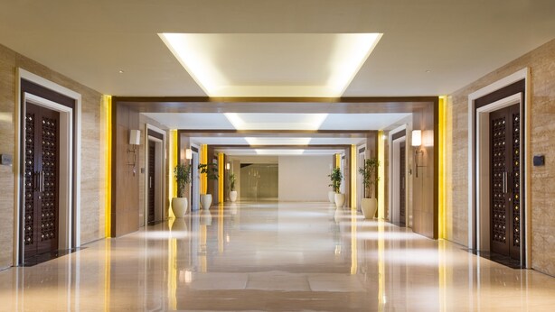 A modern hotel corridor with a reflective floor, symmetrical doorways, and recessed lighting. - Grand Mercure Solo Baru (Grogol)