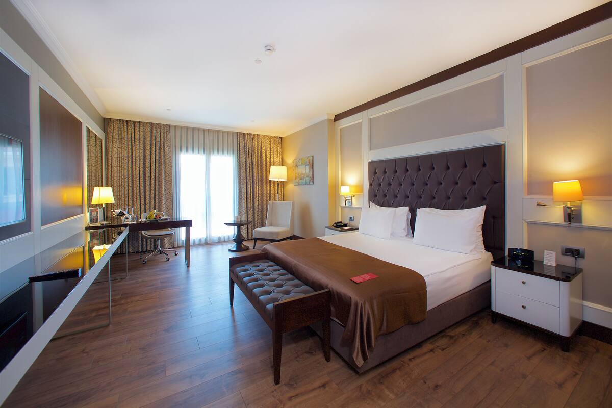 A hotel room with a large bed, a desk, a chair, and a bench.