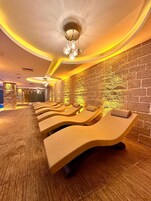 A spa room with multiple sun loungers, a stone wall, and a ceiling light fixture.