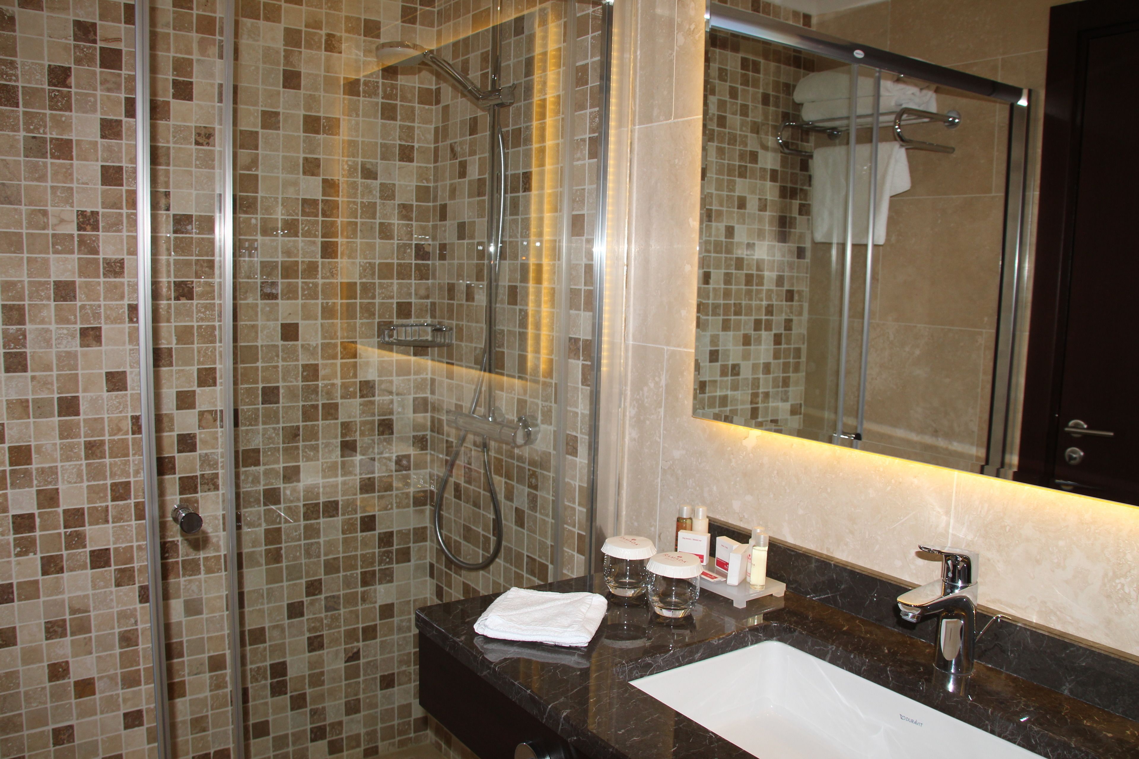 A bathroom with a glass-enclosed shower, a sink with a mirror, and toiletries on the counter.