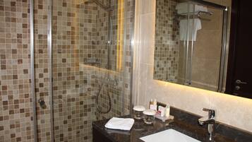 A bathroom with a glass-enclosed shower, a sink with a mirror, and toiletries on the counter.