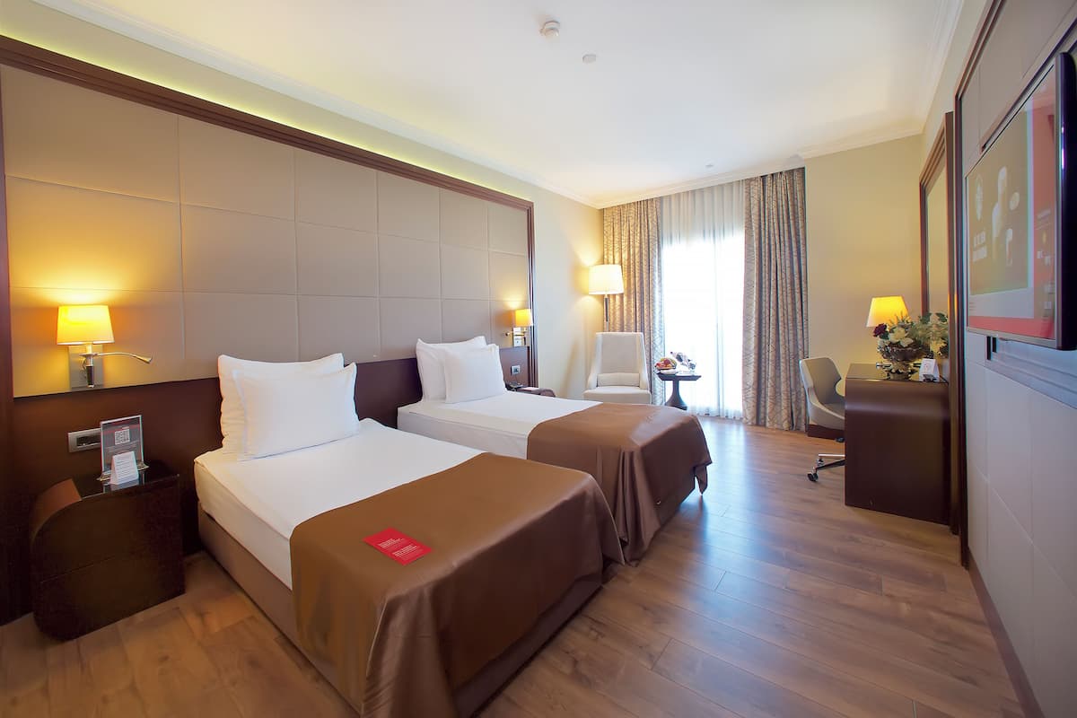 A hotel room with two beds, a desk, a chair, and a TV.