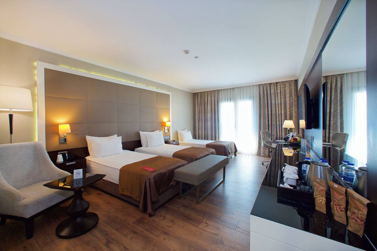 A hotel room with two beds, a sofa, a desk with a computer, a coffee machine, and a TV.