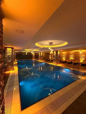 A swimming pool with a brick wall on one side and a lounge area with chairs on the other.