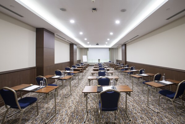 A conference room with rows of tables and chairs, a projector screen, and a whiteboard.